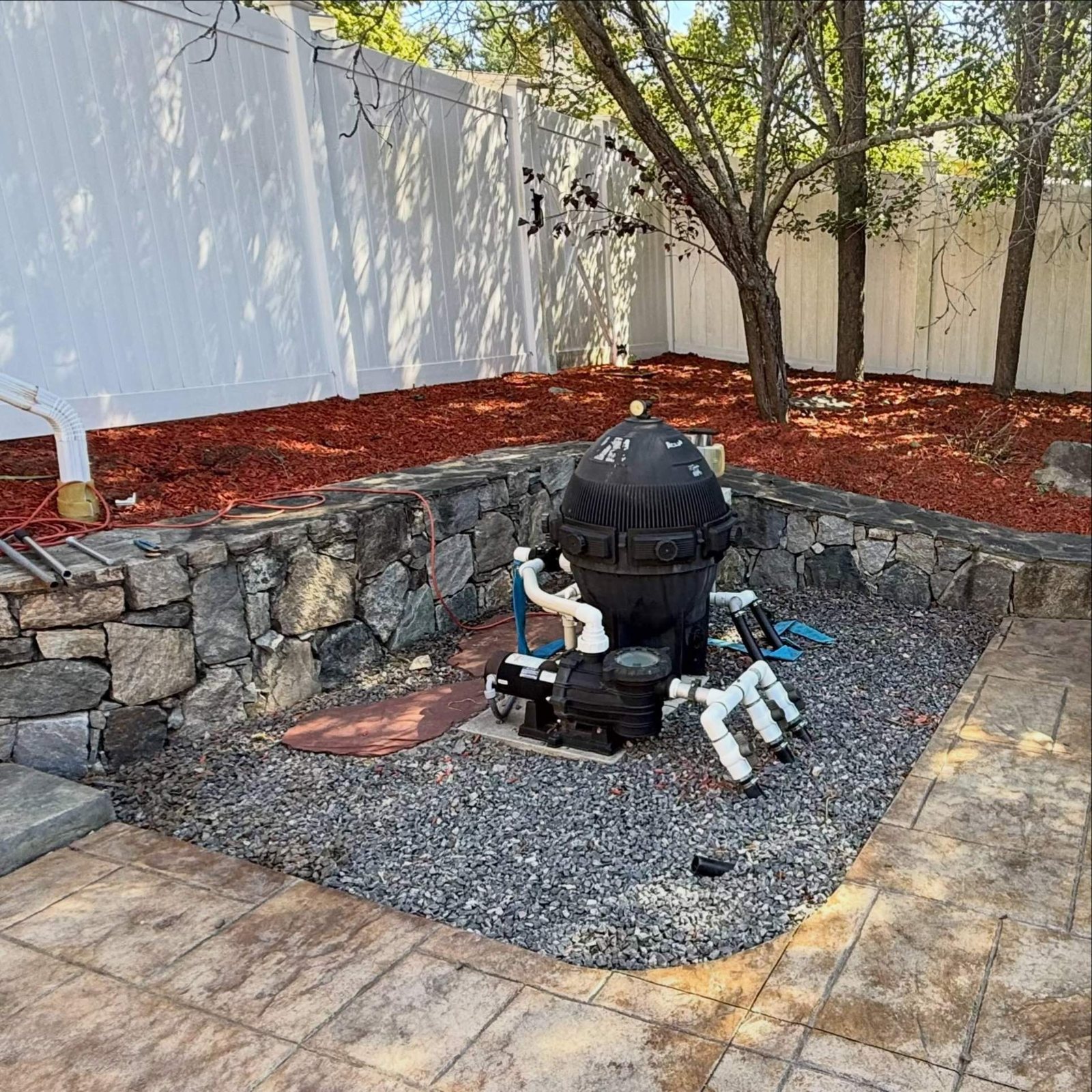 Clean pool-equipment corner with a stone wall, gravel and fresh red mulch