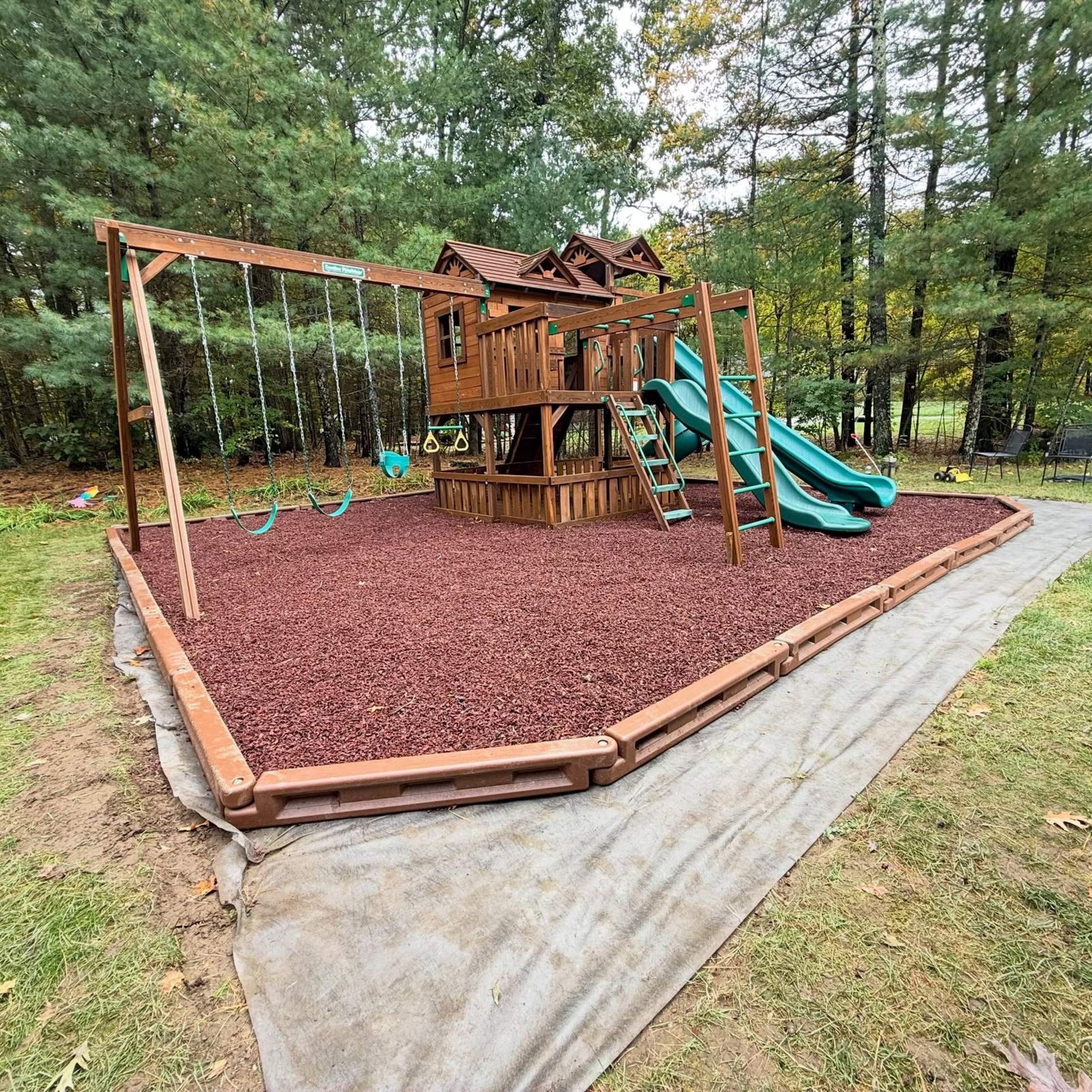 Wooden playset on a fresh bed of red playground mulch with edging